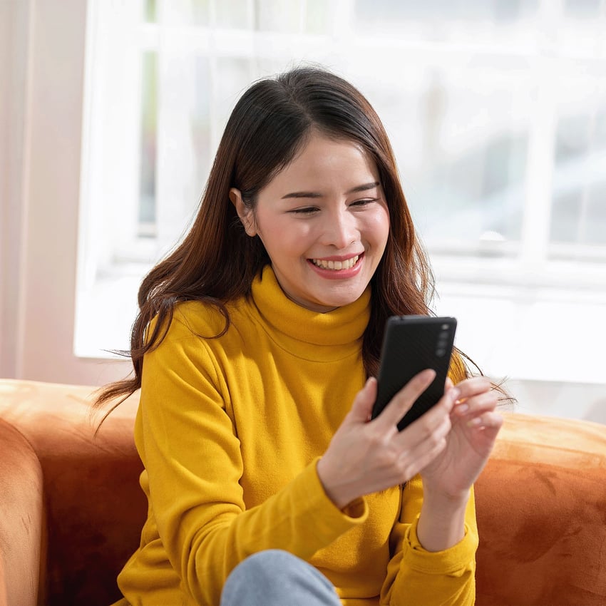 A young woman looking at her phone and smiling.