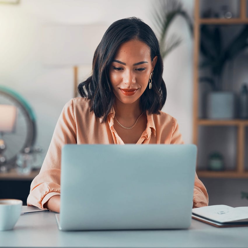 A student studying at home on a laptop with a notebook and coffee nearby.
