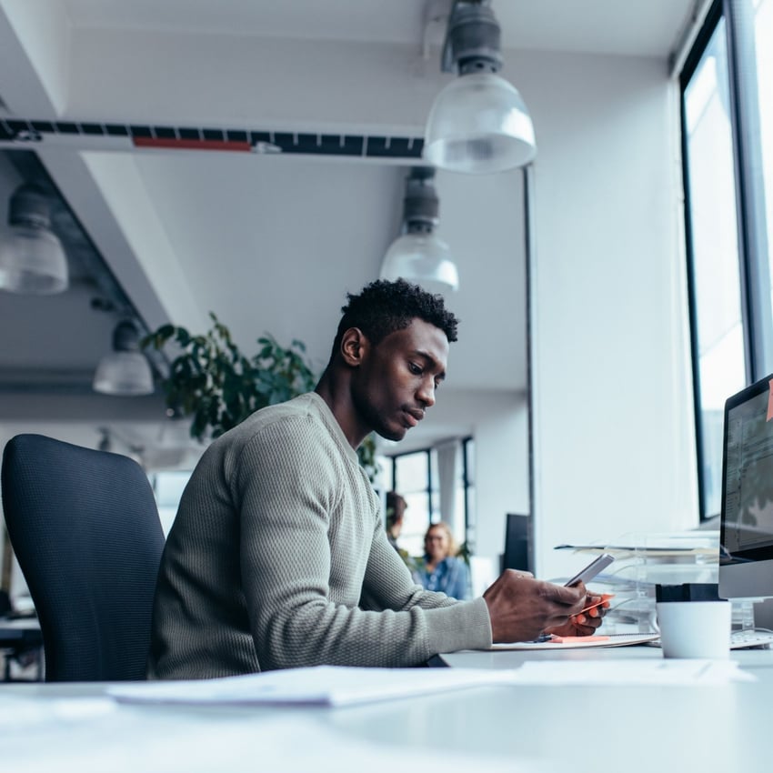 Man looking at his phone whilst at his desk