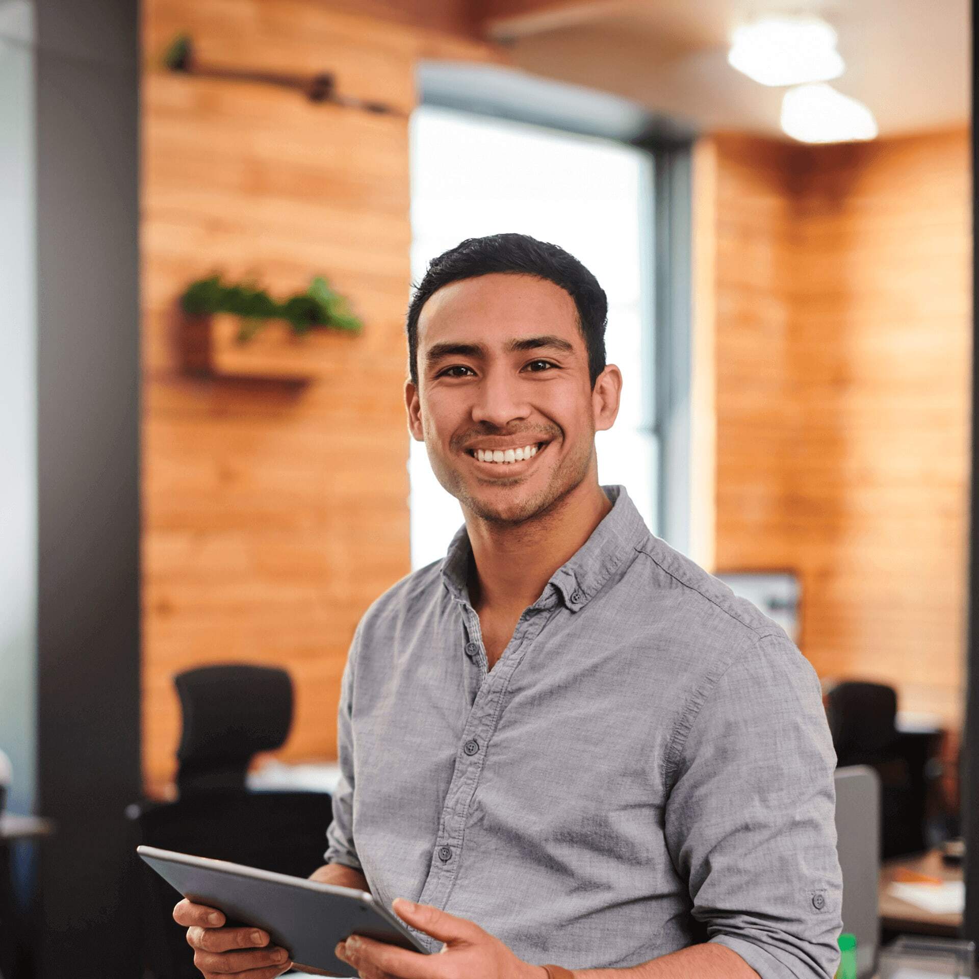 Professional man in grey shirt stands in modern office smiling at camera