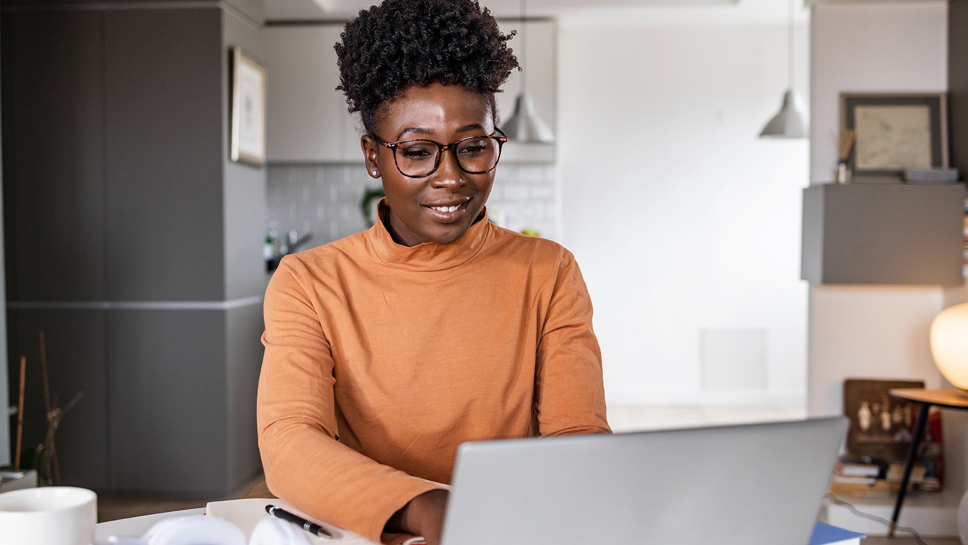 A student working on a laptop at home, focused and smiling in a modern living space.