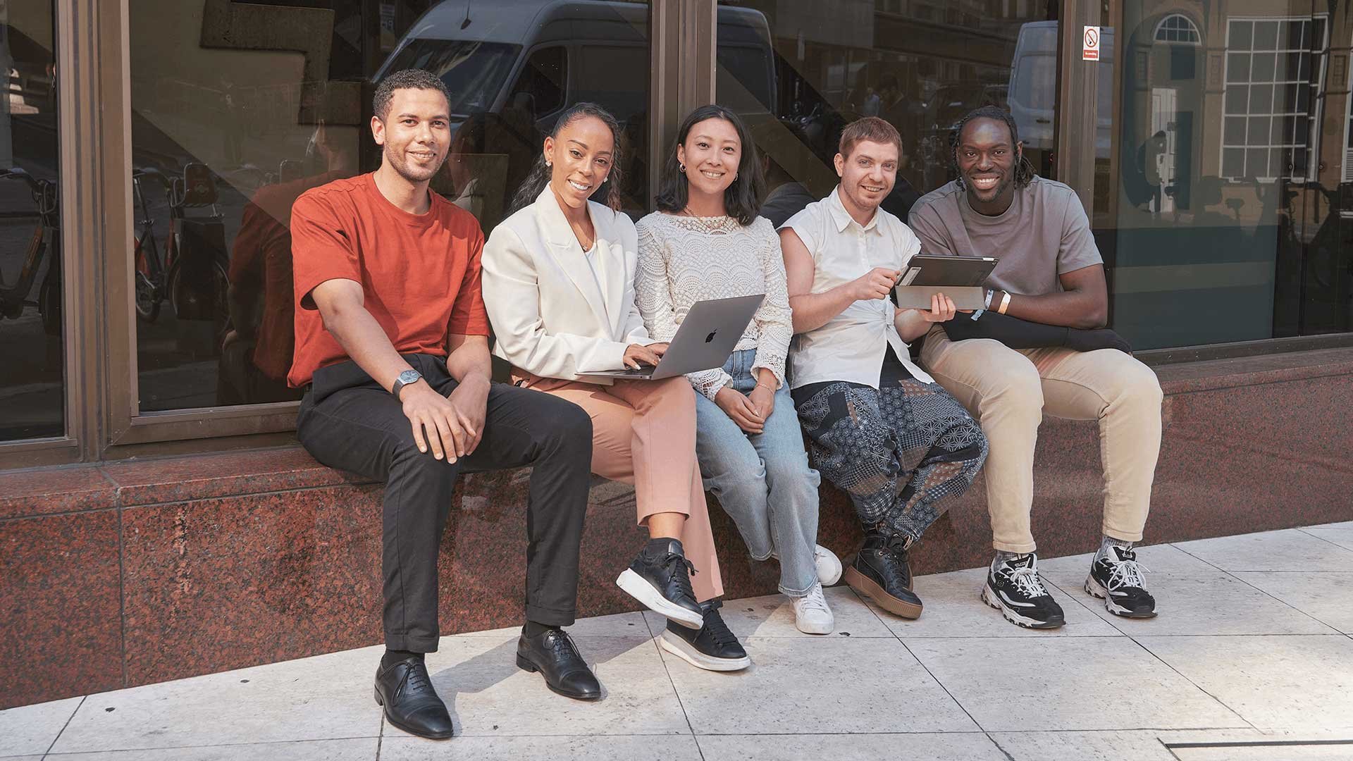 Group shot of students sitting on wall outside Walbrook campus building in London.