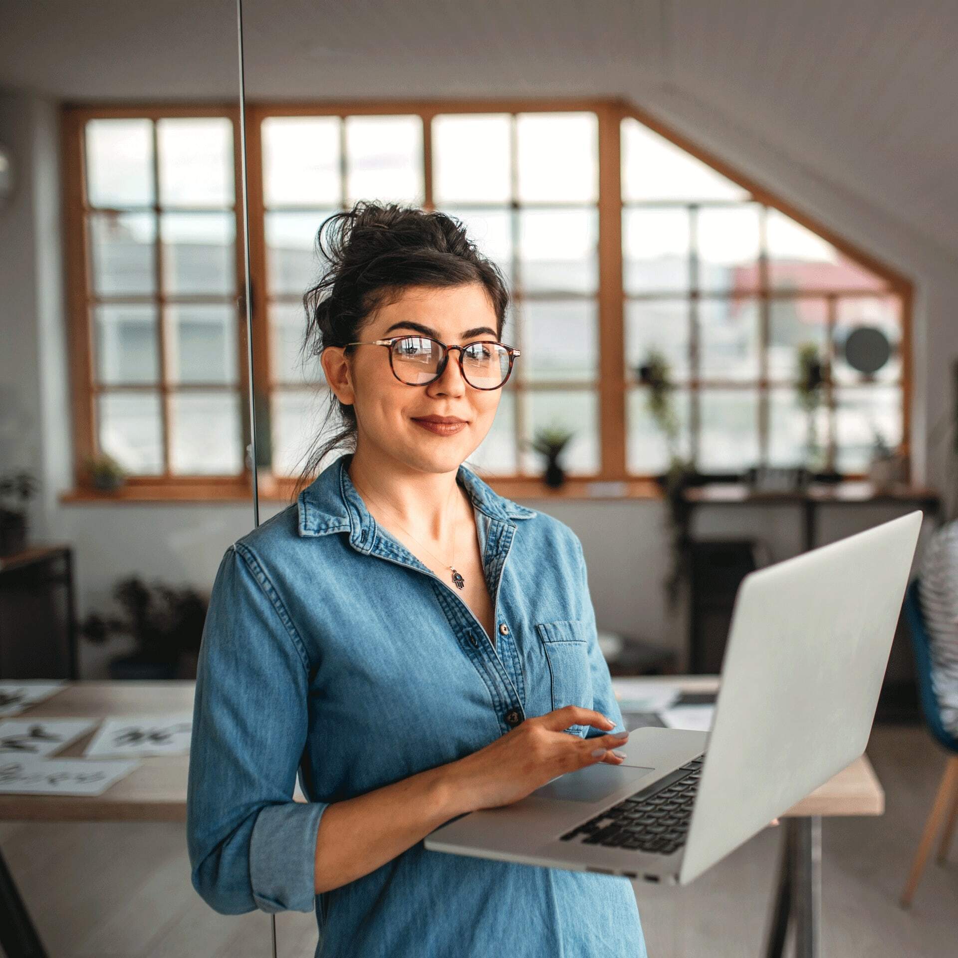 Woman studying AI online in blue shirt holds laptop in home office