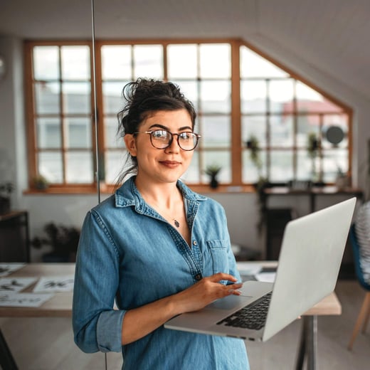 Woman studying AI online in blue shirt holds laptop in home office