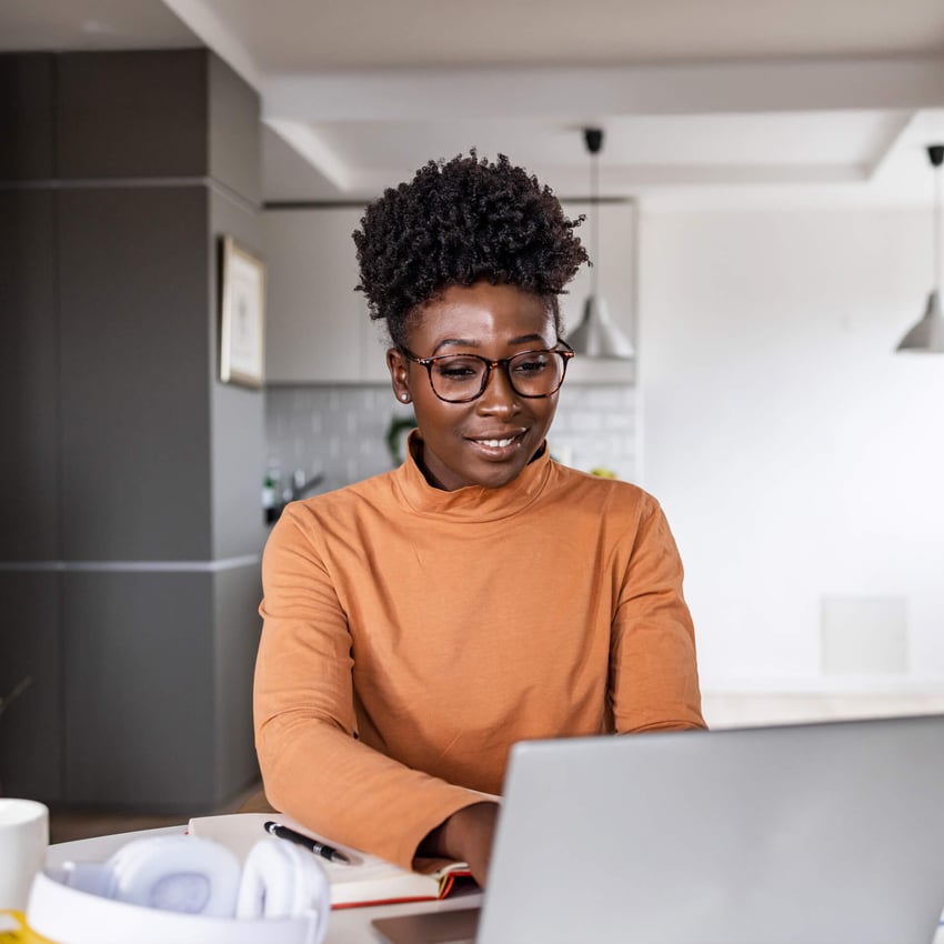 A woman smiling while looking at a laptop, studying artificial intelligence and data science online.