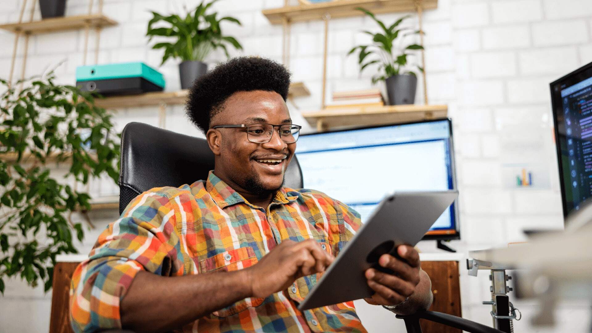 Man in colourful check shirt and glasses using AI on a tablet to help his job as a marketing specialist.