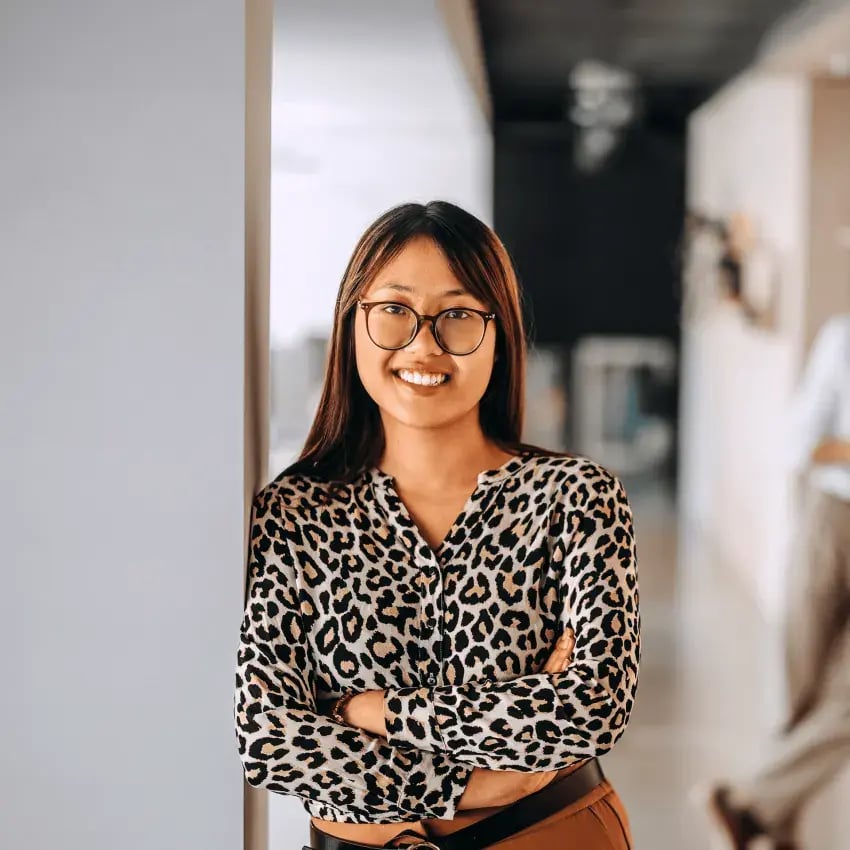 Woman in leopard print shirt stands cross armed smiling at camera