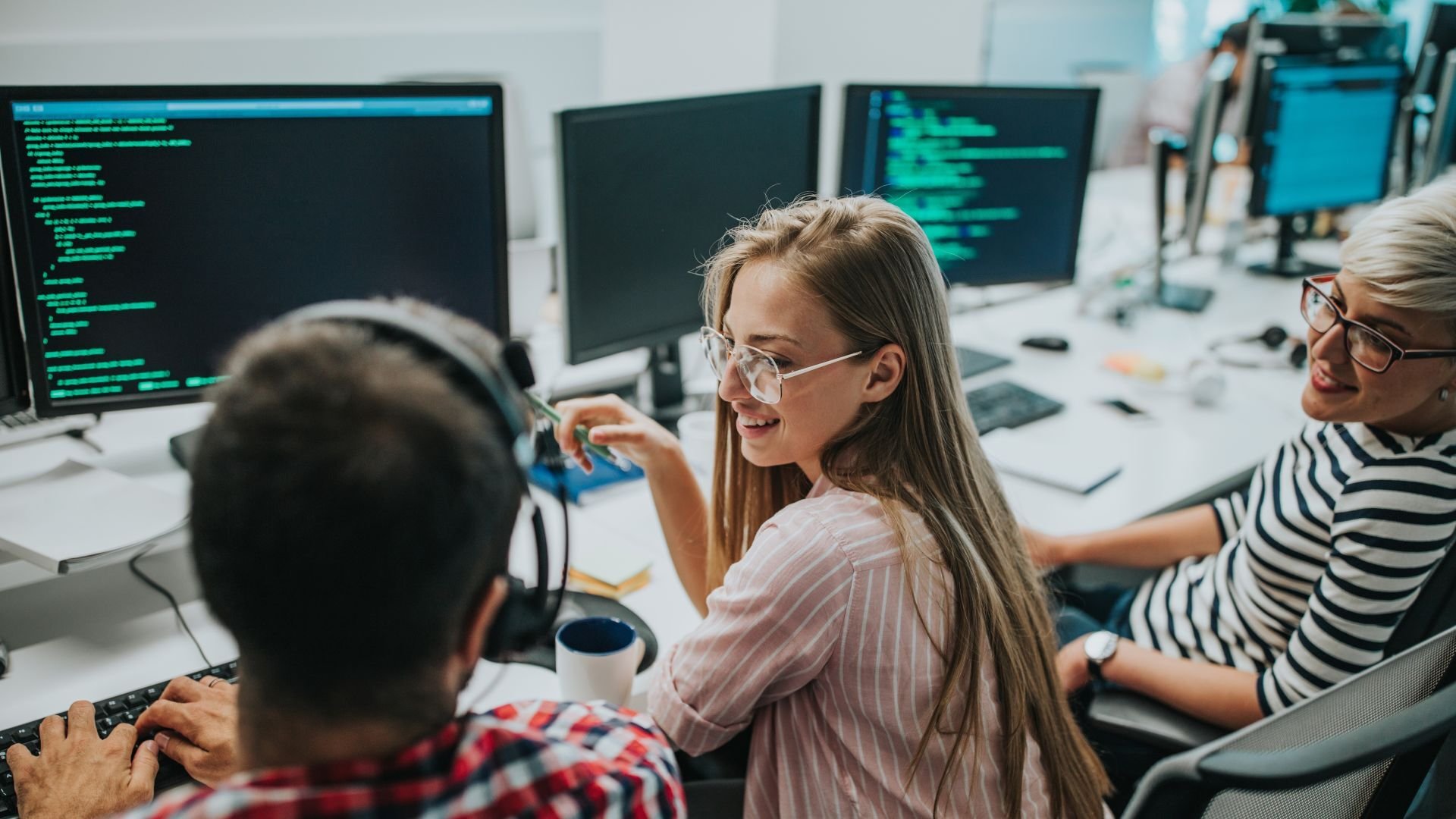 Woman talking with coworkers in front of computer screens displaying code