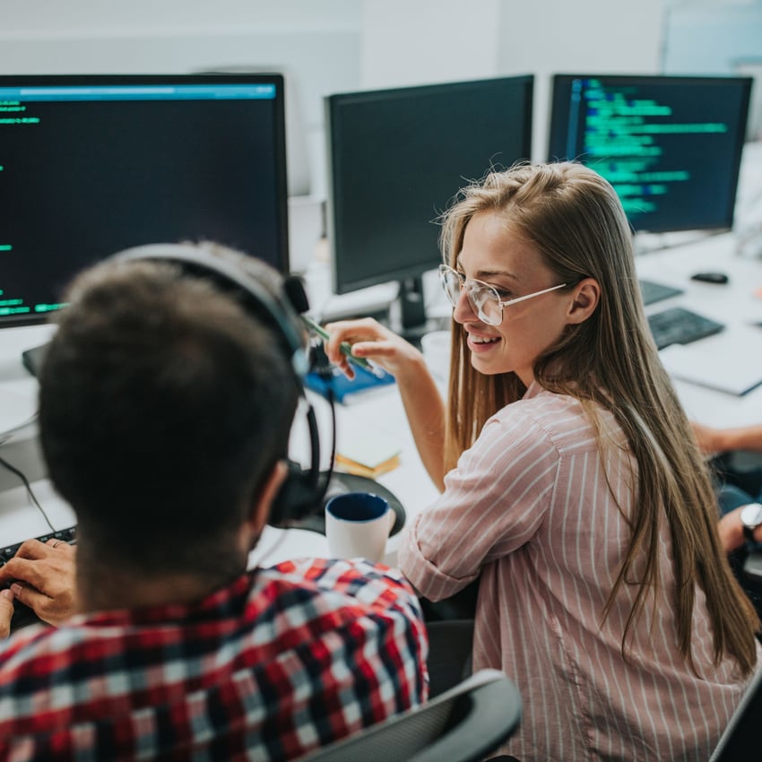Woman talking with a coworker in front of computer screens displaying code