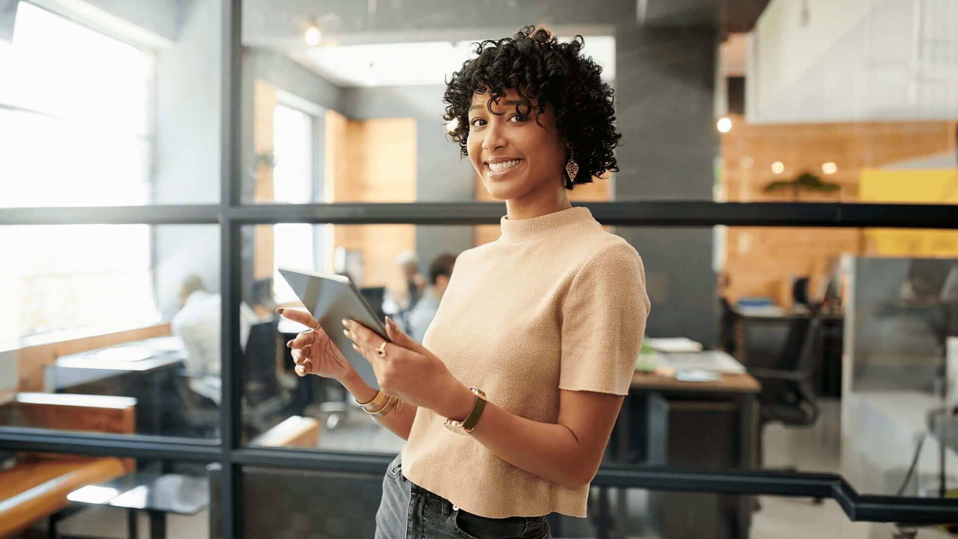 Curly hair woman stands in organization office holding tablet that holds a data report.