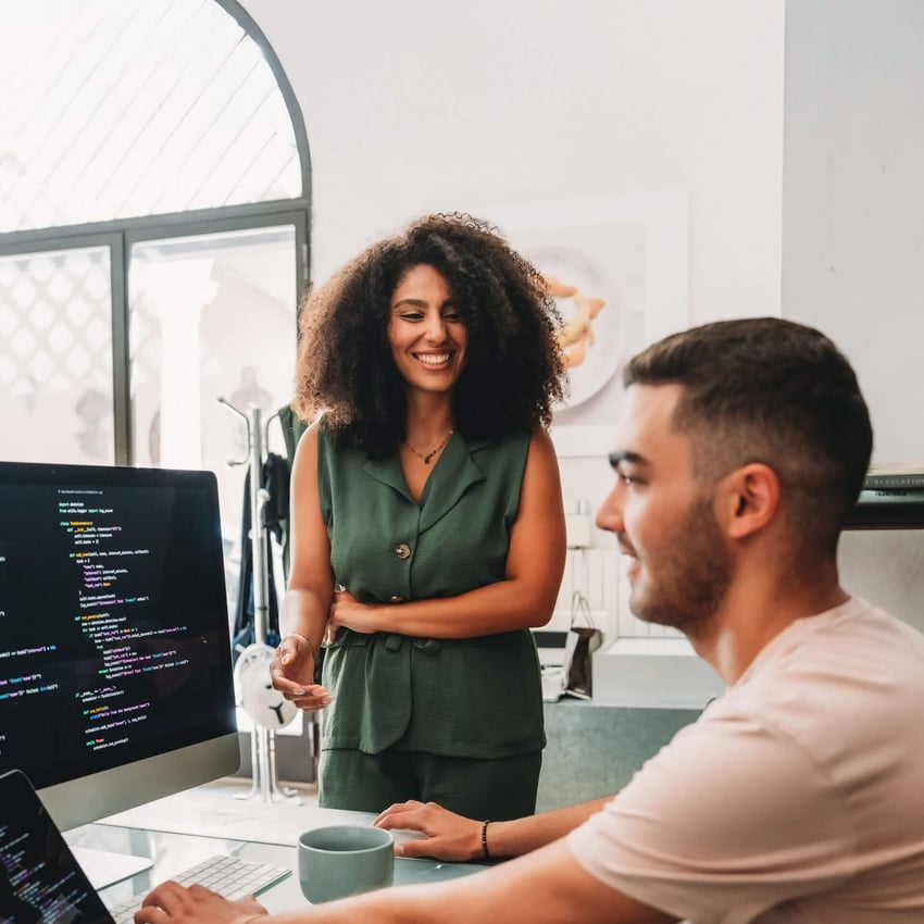 Female computer scientist working in office with male computer scientists who is coding at desk