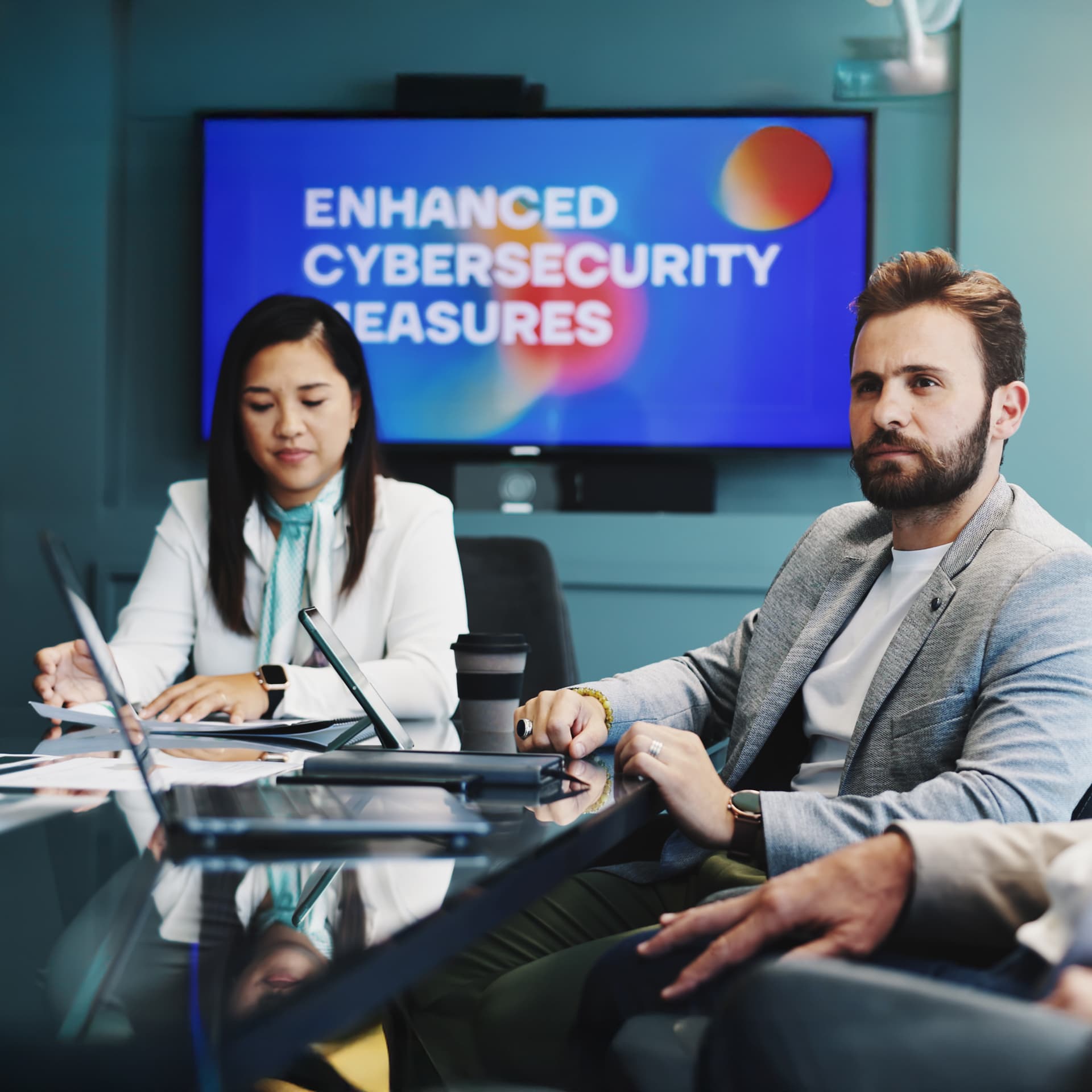 Man in grey blazer sat with colleagues in a meeting about cyber security.