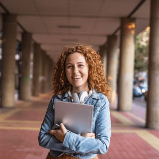 Smiling student outside holding laptop and smiling at camera.