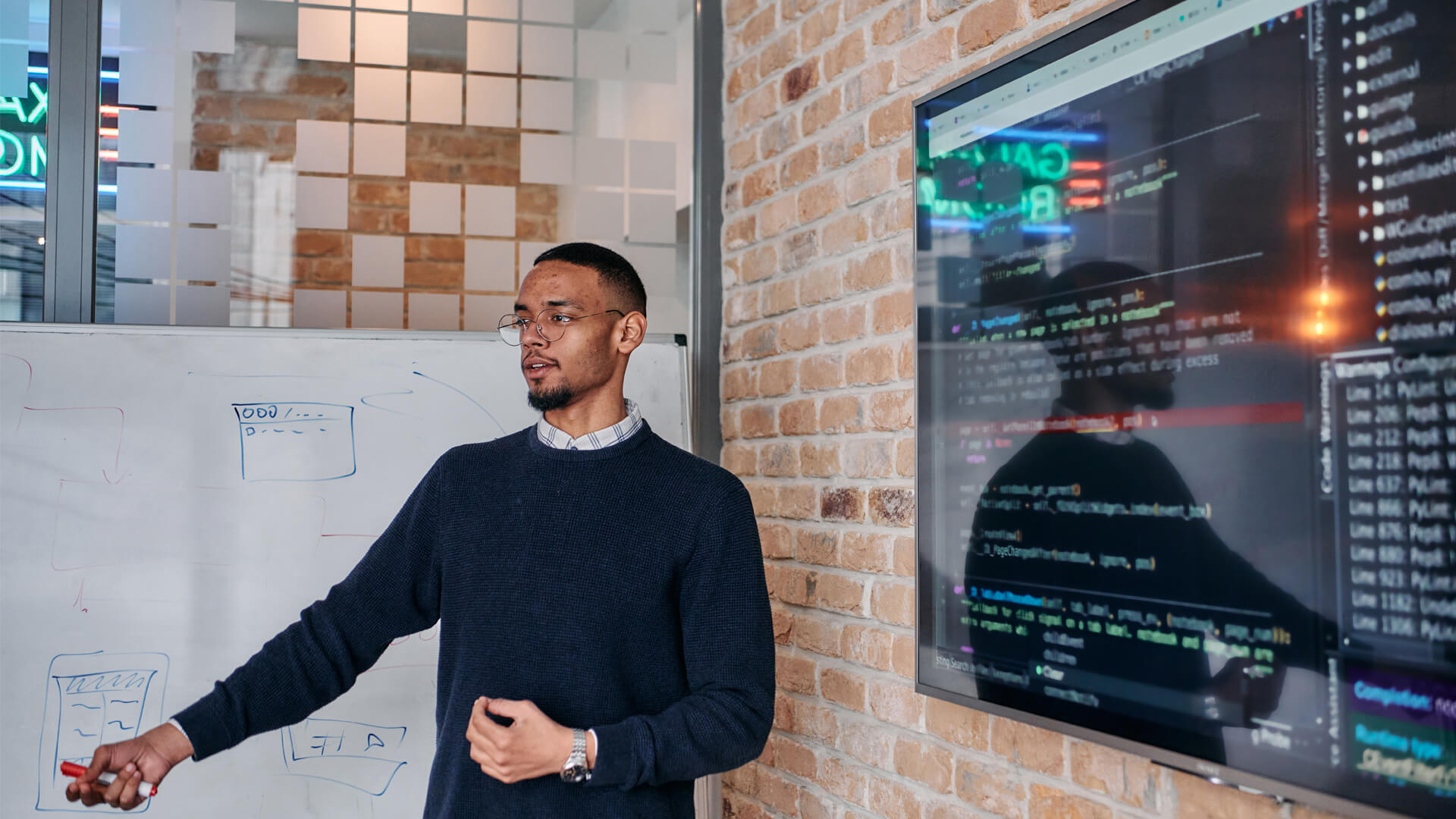 Young professional demonstrating programming on a screen in a modern office.