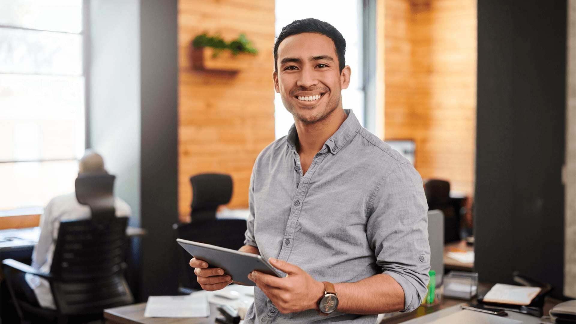 Smiling man in grey shirt holds tablet, preparing data for organization wide meeting.