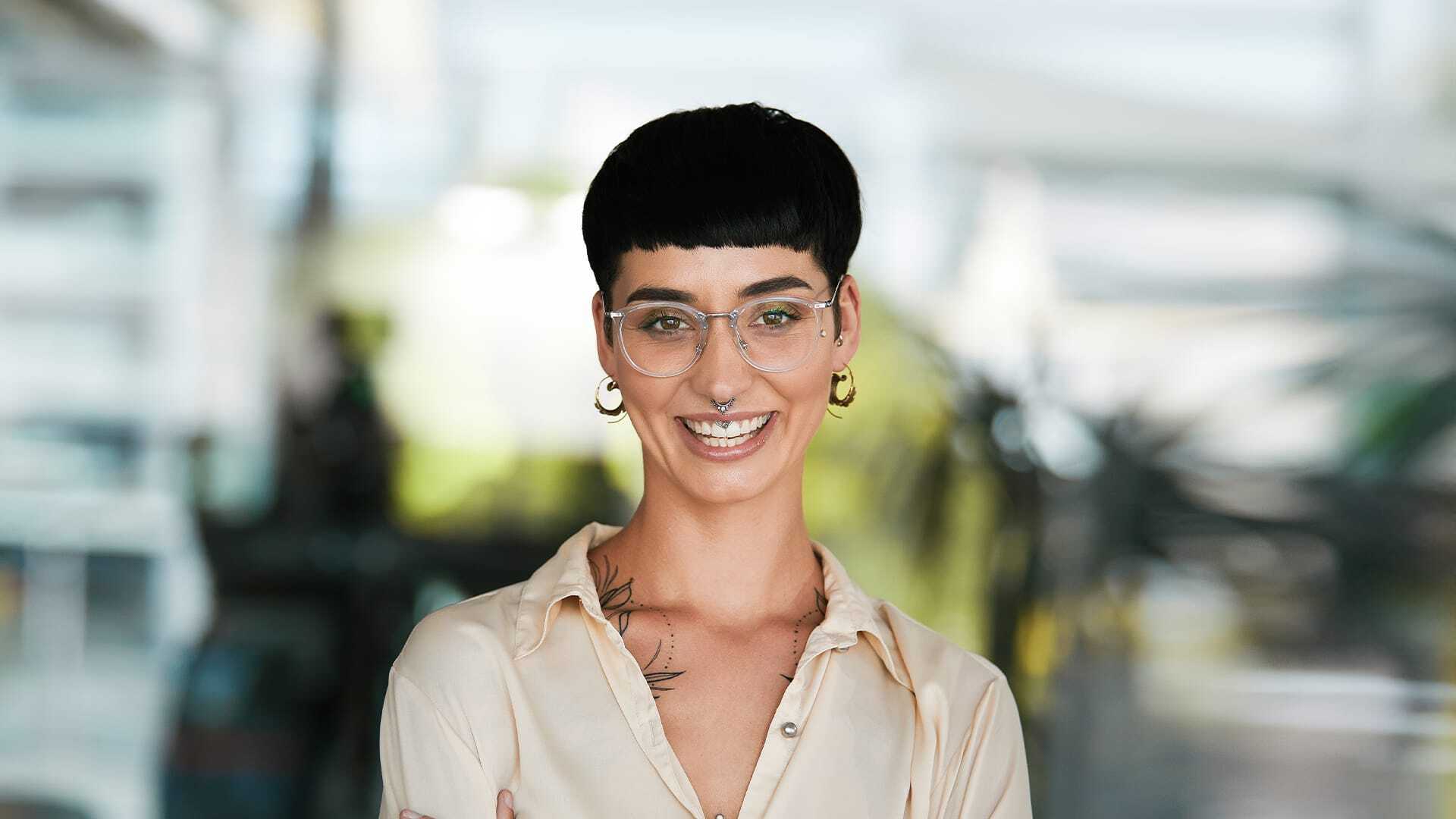 Woman in short hair, bangs, glasses and piercings stands in modern office, using her business intelligence ability.