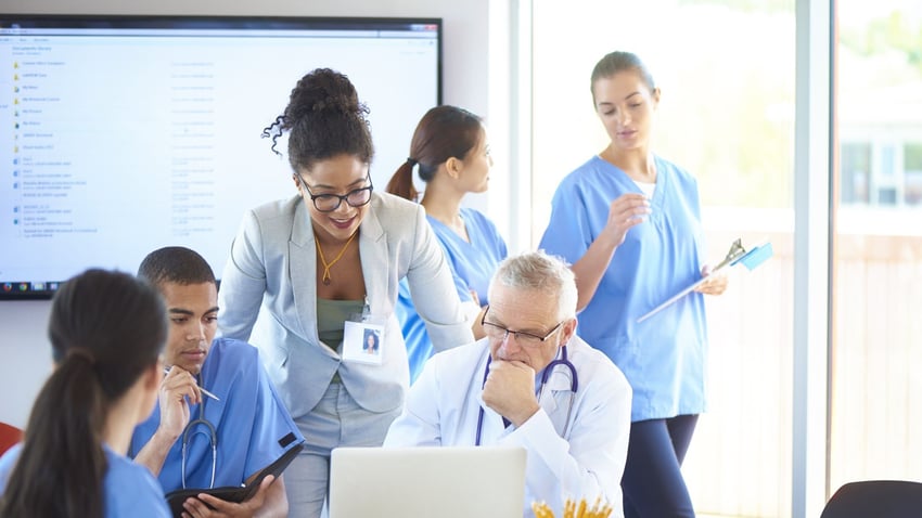 Group of coworkers in medical setting gathered around a laptop