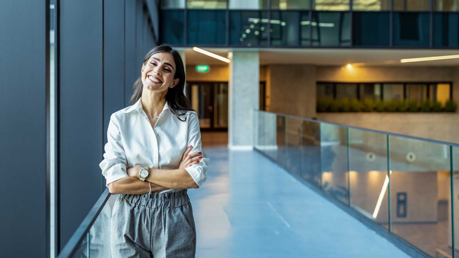 Professional online MBA graduate standing with crossed arms in a modern office.