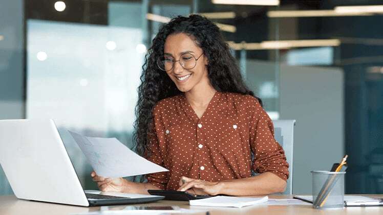 Happy businesswoman at laptop in office reviewing full-time job applications from MBA graduates.