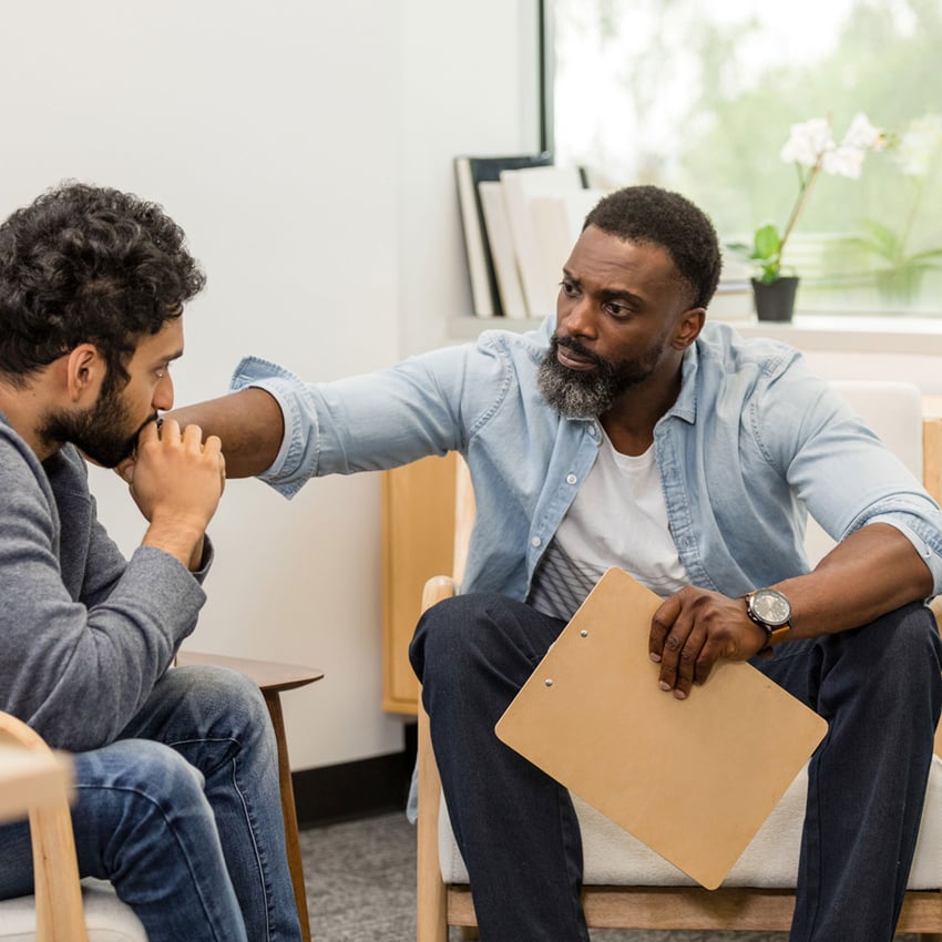 Male psychologist comforts someone in a meeting.