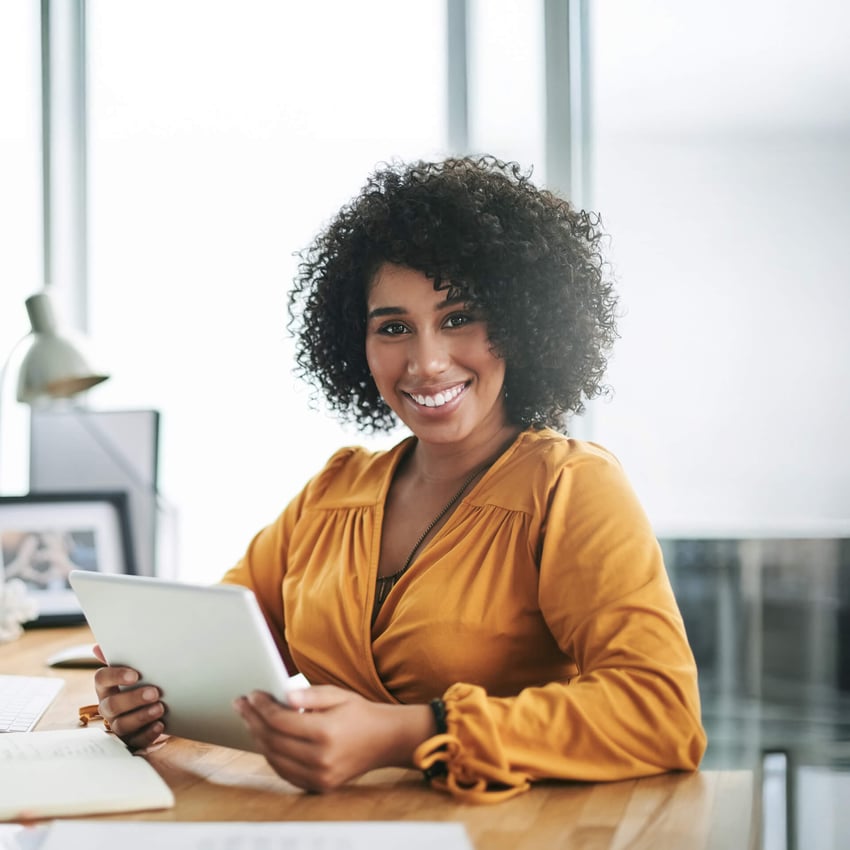 Woman in yellow shirt holds tablet at desk