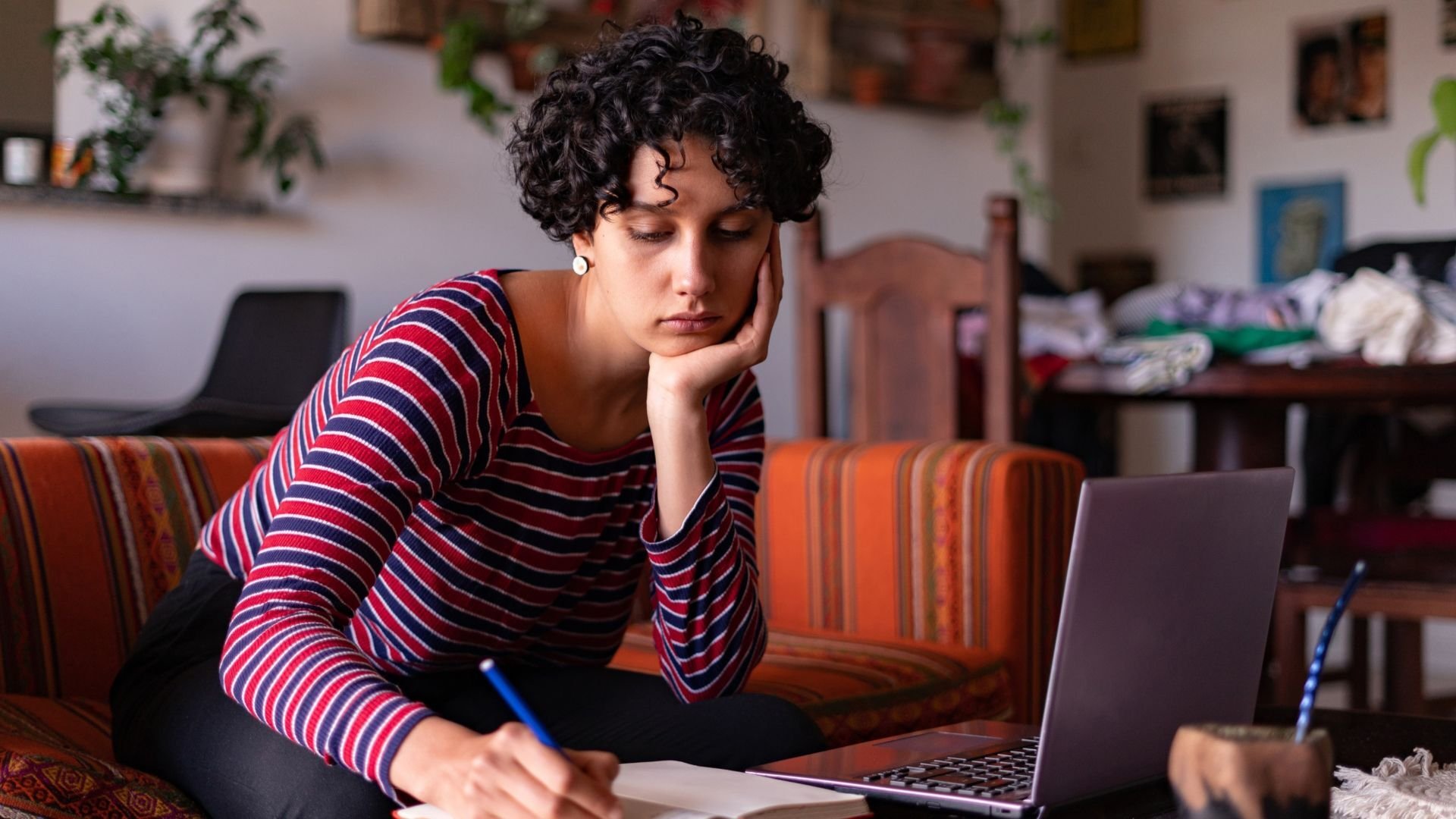 Woman studying on her laptop and taking notes on a notepad