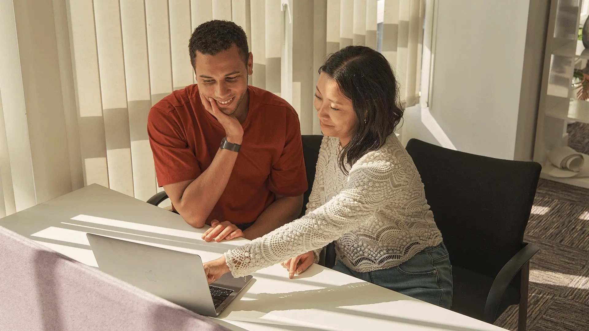 A man and woman sat smiling at a laptop screen, attending an online Walbrook webinar