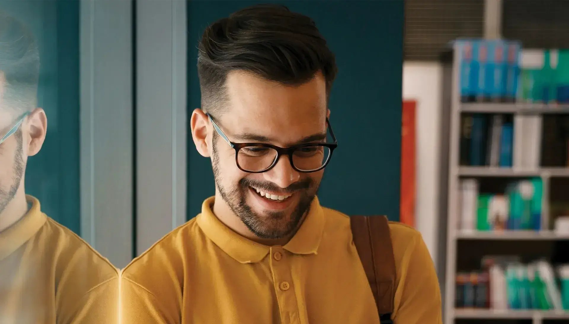 Young man wearing glasses standing, holding an ipad smiling.