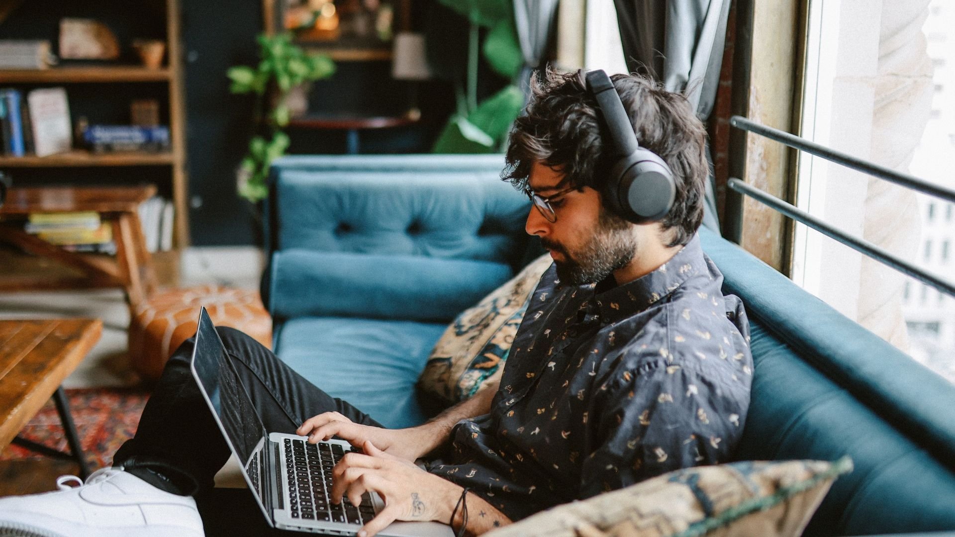 Man wearing headphones and using a laptop on the sofa