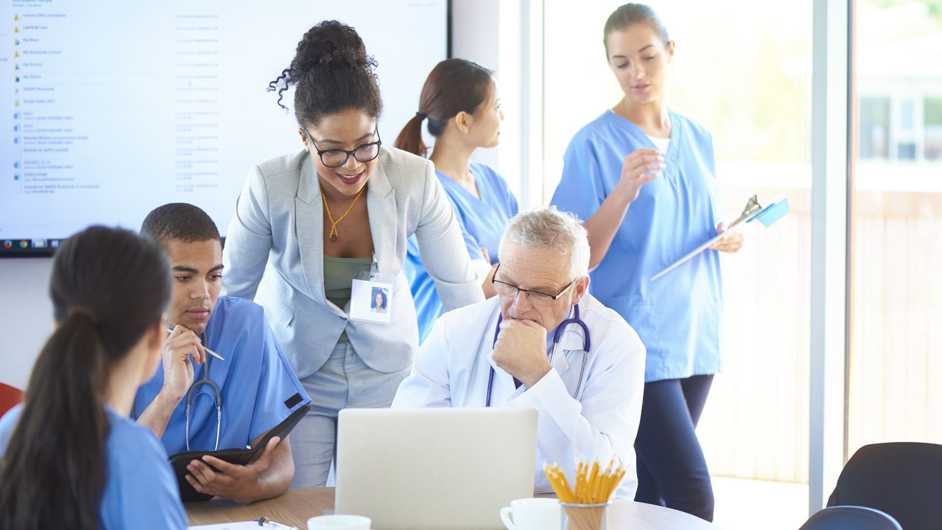 Group of employees in medical facility gather round laptop