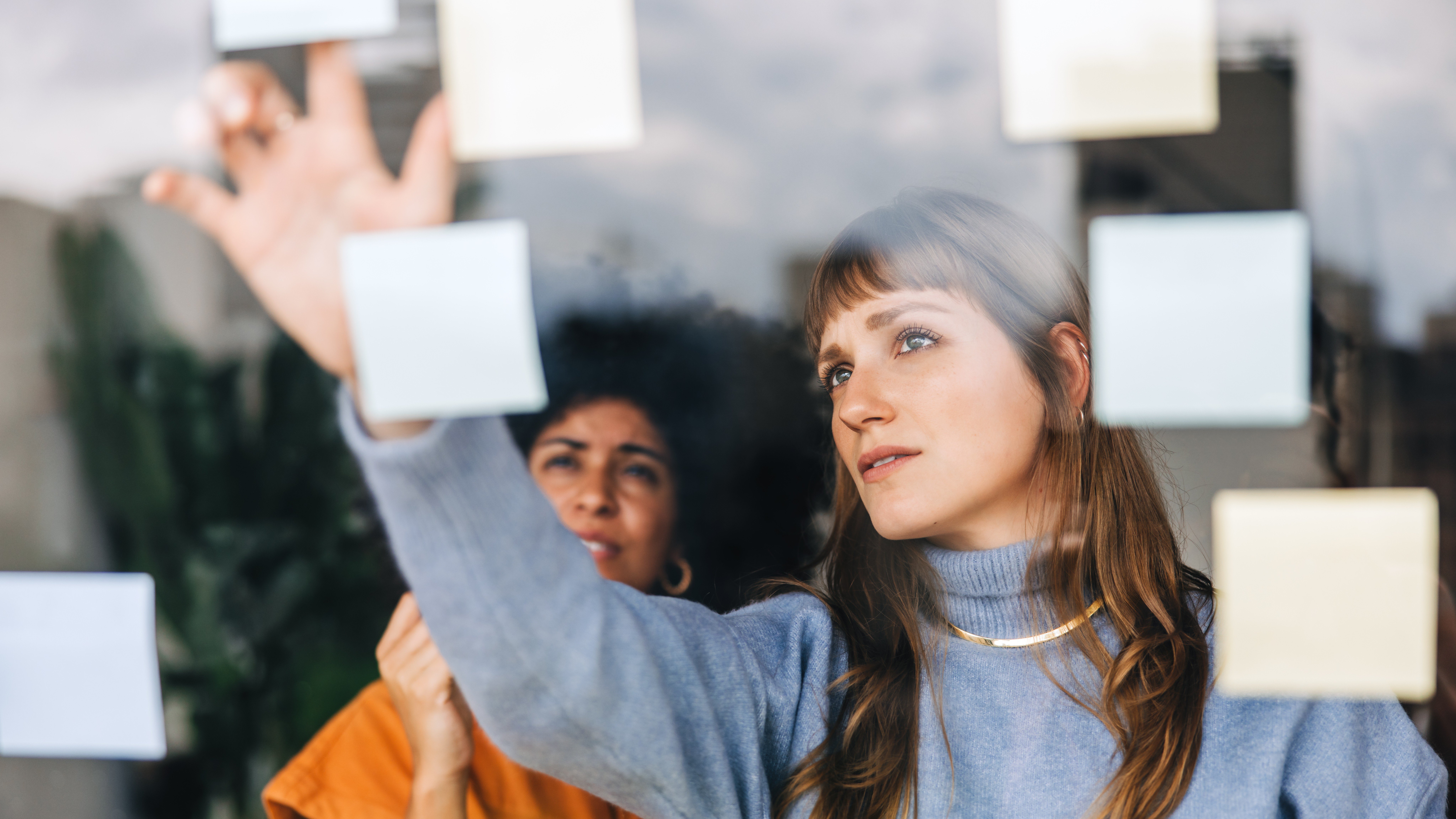 Two woman discussing and using sticky notes on a wall