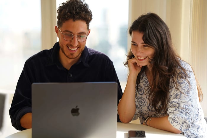Two young students sat at a table, smiling whilst looking into student support services