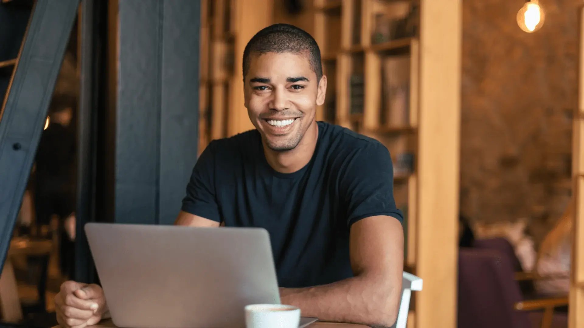 Smiling man with laptop in a café researching further study opportunities for finance graduates.