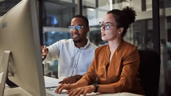 Online MBA graduate shares AI strategies with a peer during a workplace session in a tech-driven office.