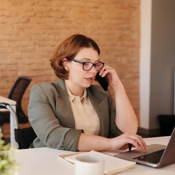 Woman with glasses sitting at her desk with her computer and talking on the phone.