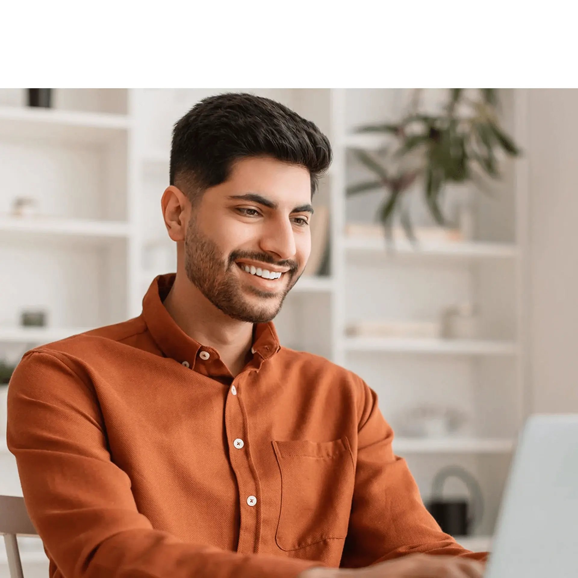 Young smiling man wearing an orange shirt, typing on his laptop.