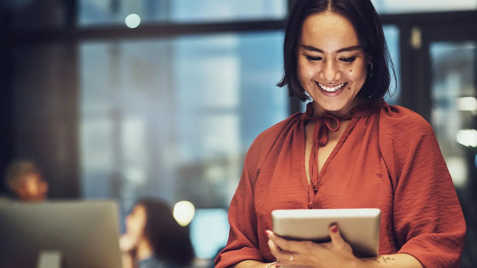 A woman standing, looking at her ipad and smiling.
