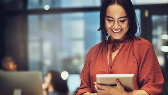 A woman standing, looking at her ipad and smiling.
