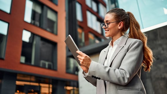 A young woman standing outside with her ipad and smiling.