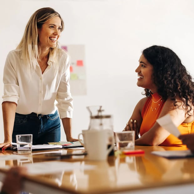 Woman standing smiling and a young woman sitting smiling.