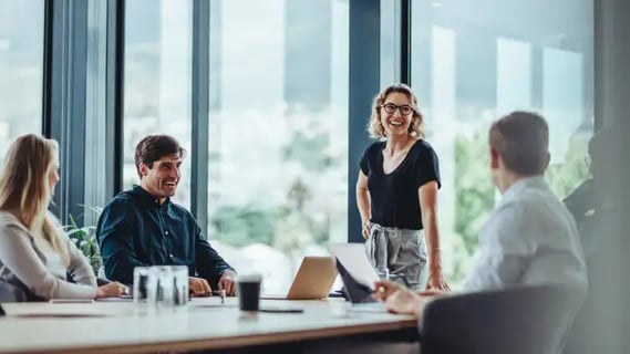 Smiling MBA Finance graduate inspires her team during a planning session in a light-filled modern office.
