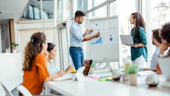 Online MBA graduate leads a collaborative finance meeting, explaining key data on a flipchart.