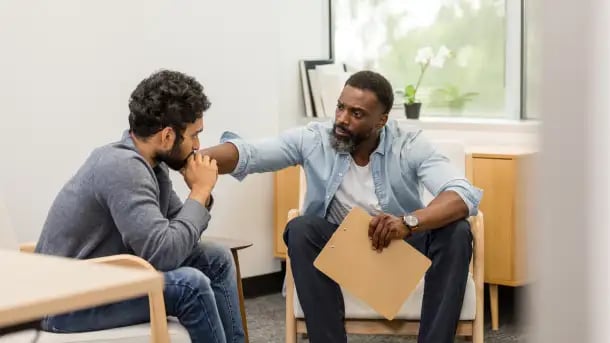 Male psychologist comforts someone in a meeting.