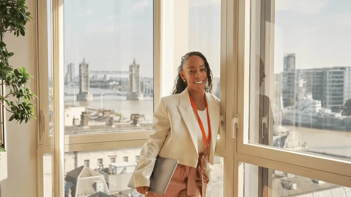 A Walbrook student in cream blazer standing at the window overlooking the River Thames, from our London campus.