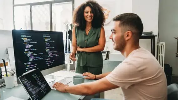 Smiling IT project manager supports young developer in a modern office at the end of their academic year.