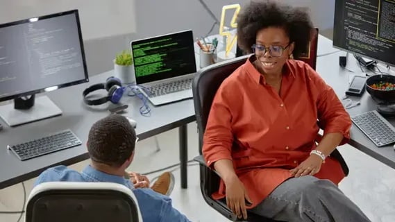Female cloud architect in orange shirt works on programming at a desk with a colleague.