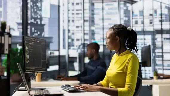 Young female engineer in yellow t-shirt works on web technologies in a modern office.