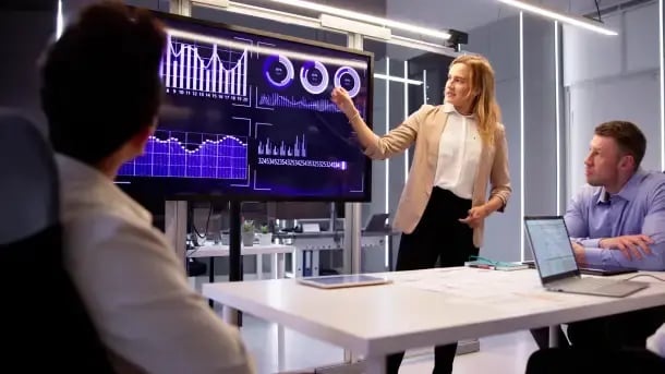 Professional woman in white shirt and blazer presents data visualisation in modern office.