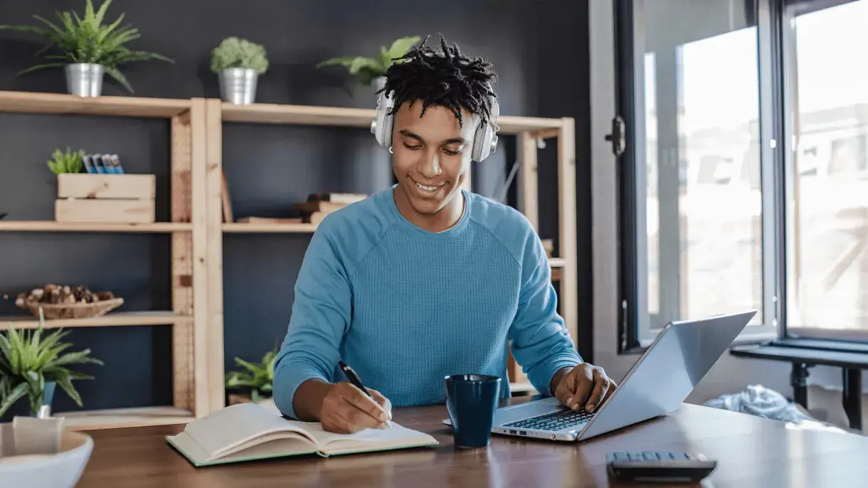 Man studying at home making notes from a laptop