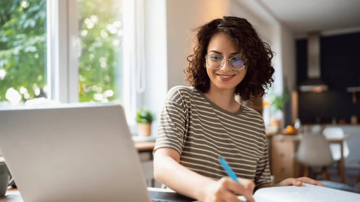 A woman sitting at a desk, smiling while working on a laptop.